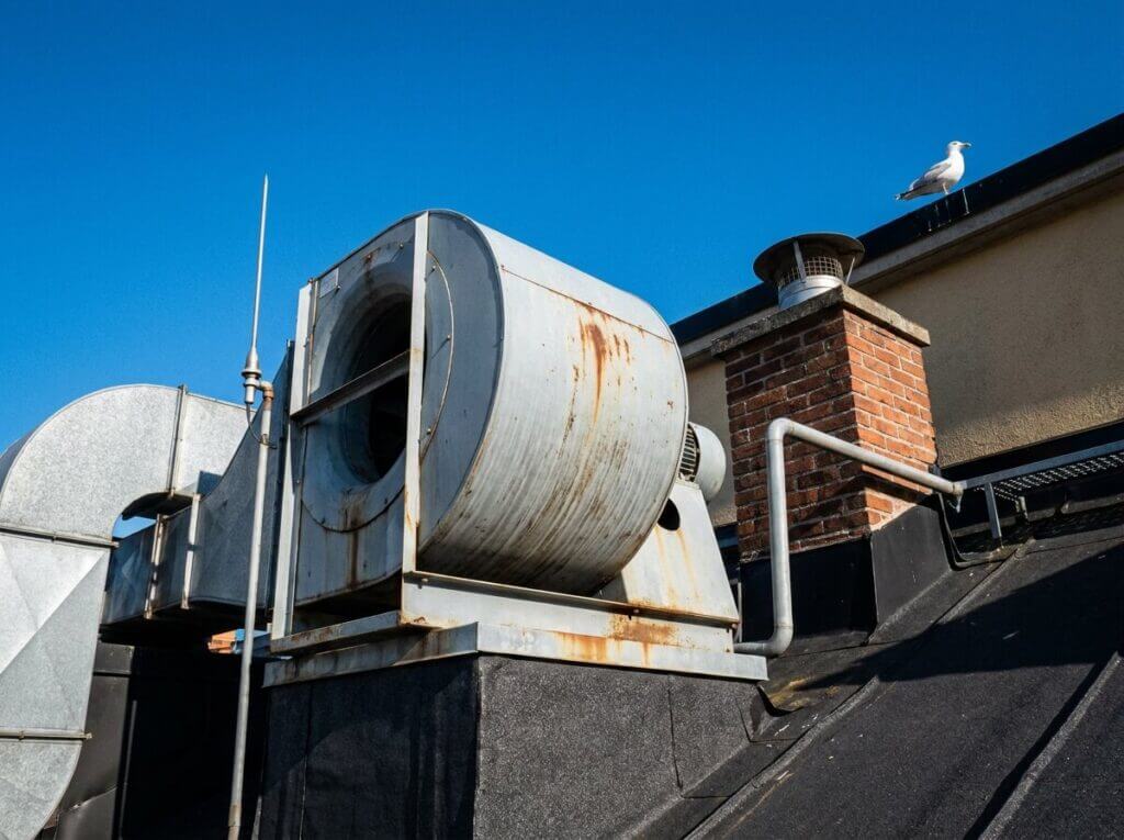 Ventilationsaggregat på tak till flerfamiljshus i Göteborg mot blå himmel — OVK kontrollerar att det fungerar